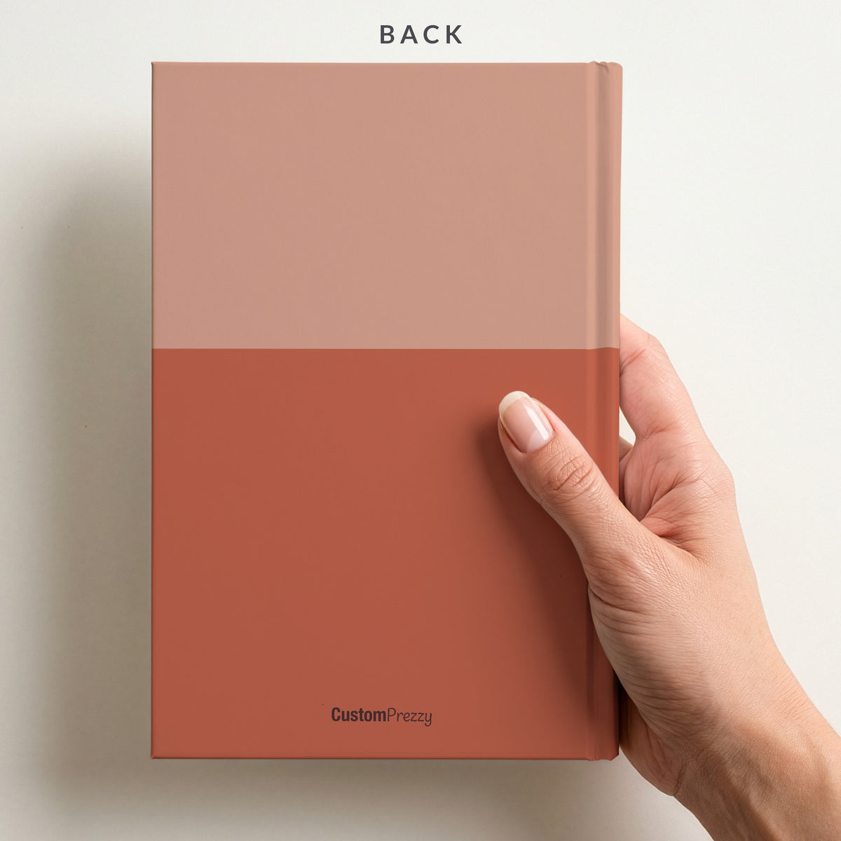 Back of the terracotta two tone notebook held in a hand, with the colour split running around the back and the Custom Prezzy wordmark at the foot