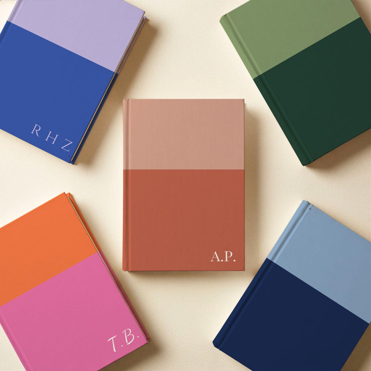 Five two tone initials notebooks in sage and pine, lilac and cobalt, orange and pink, sky and navy, and terracotta