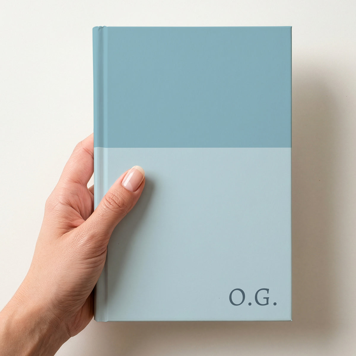 Hand holding a duck egg two tone personalised notebook with the initials O.G. in Alegreya in the lower corner