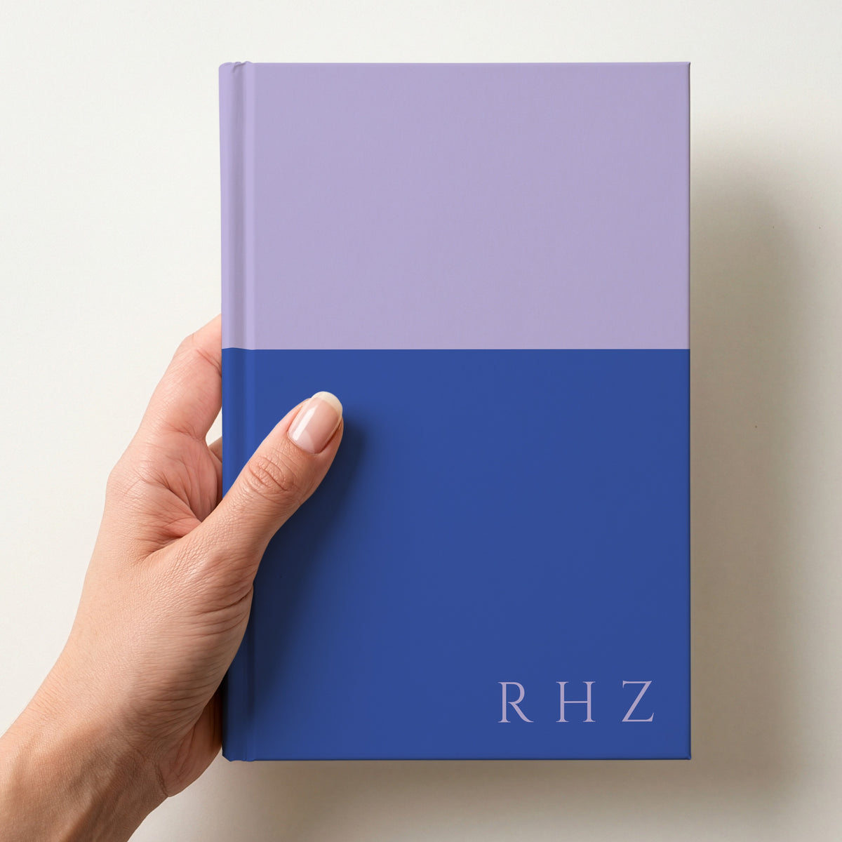 Hand holding a lilac and cobalt two tone personalised notebook with the initials RHZ in Cinzel in the lower corner
