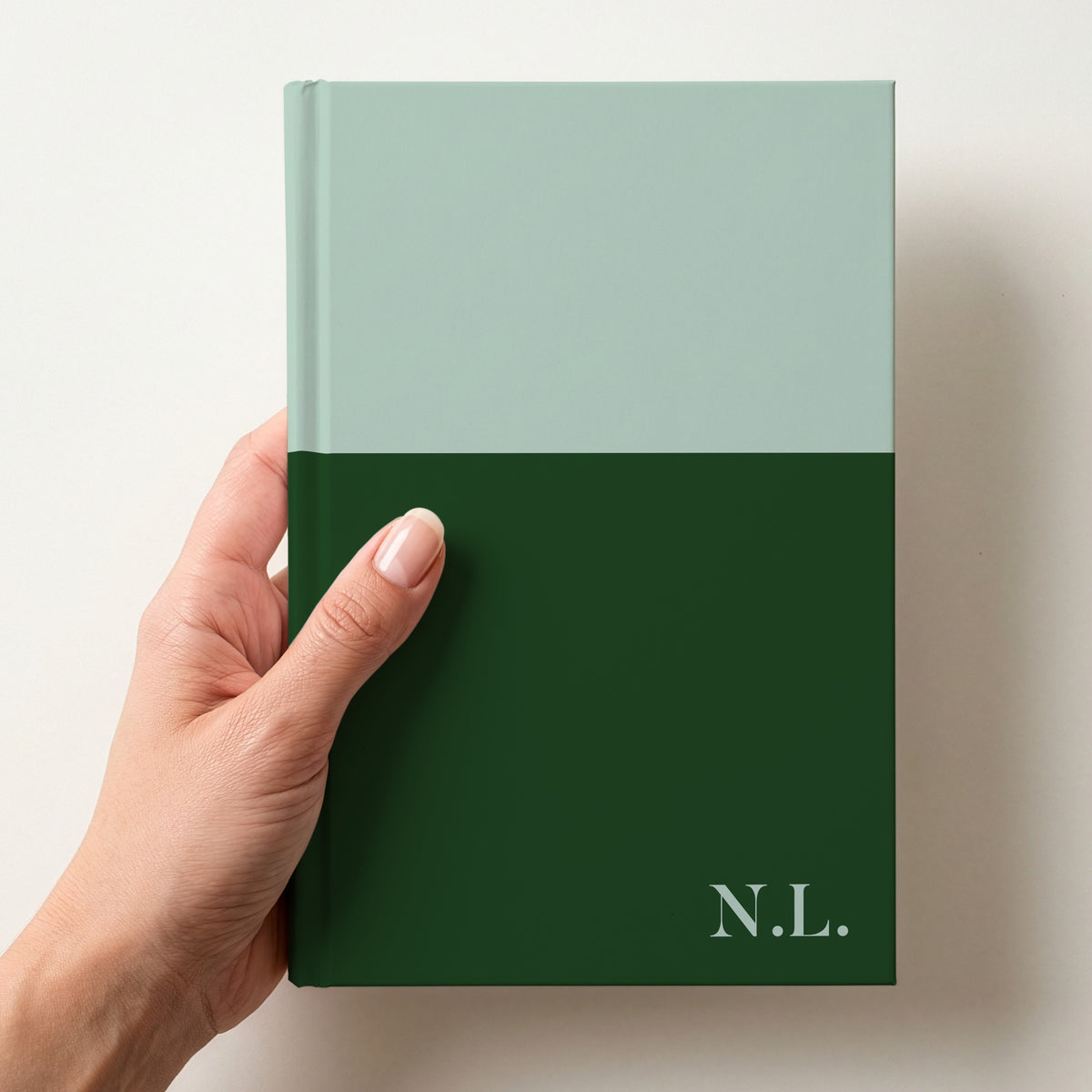 Hand holding a mint and bottle two tone personalised notebook with the initials N.L. in Butler in the lower corner