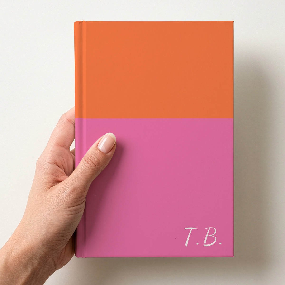 Hand holding a orange and pink two tone personalised notebook with the initials T.B. in Dancing Script in the lower corner