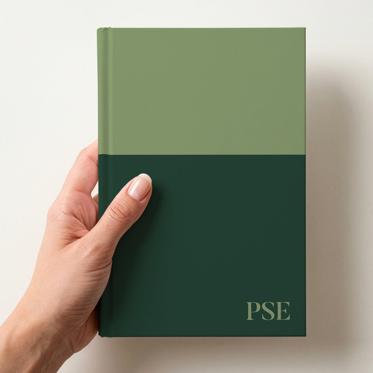 Hand holding a sage and pine two tone personalised notebook with the initials PSE in Butler in the lower corner