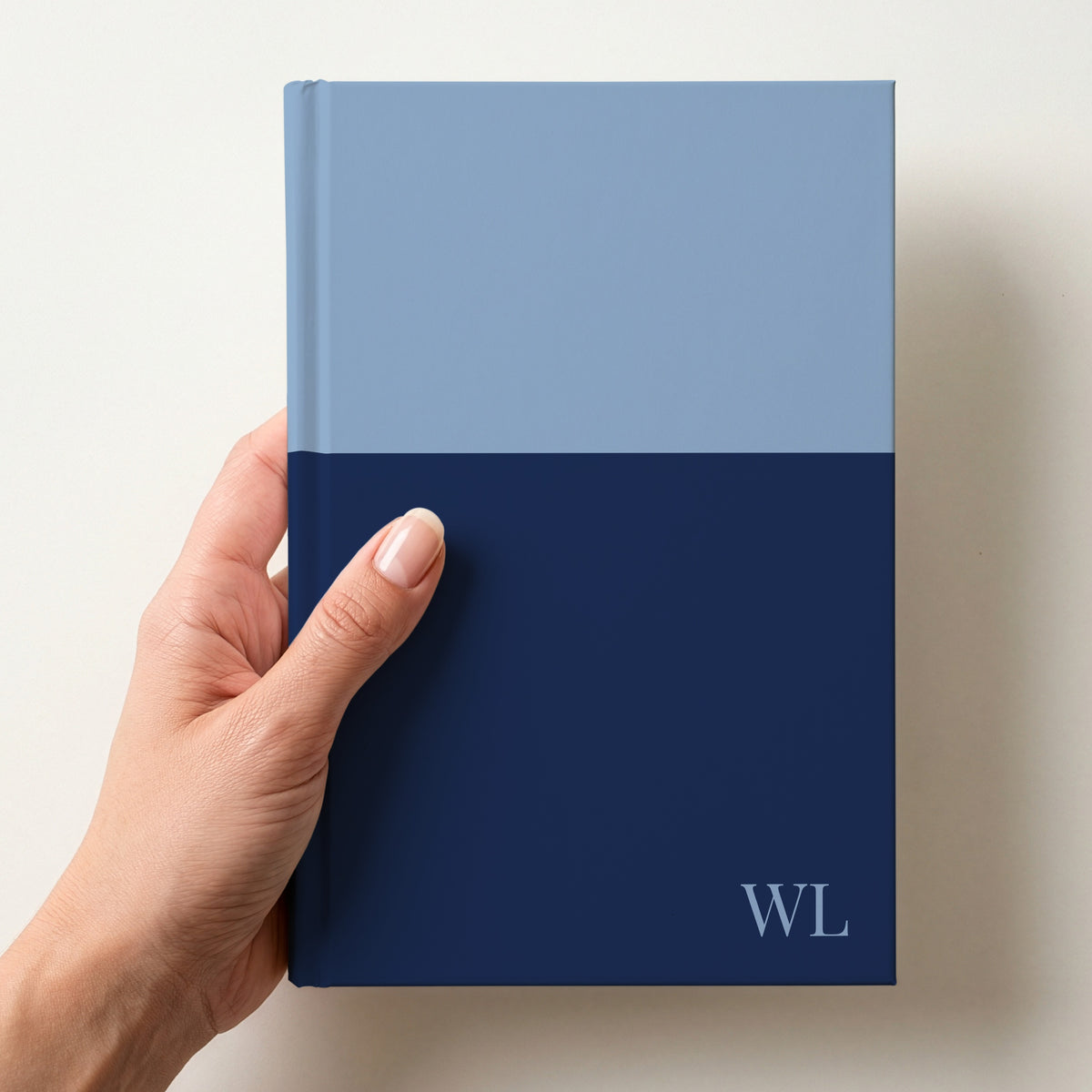 Hand holding a sky and navy two tone personalised notebook with the initials WL in Playfair Display in the lower corner