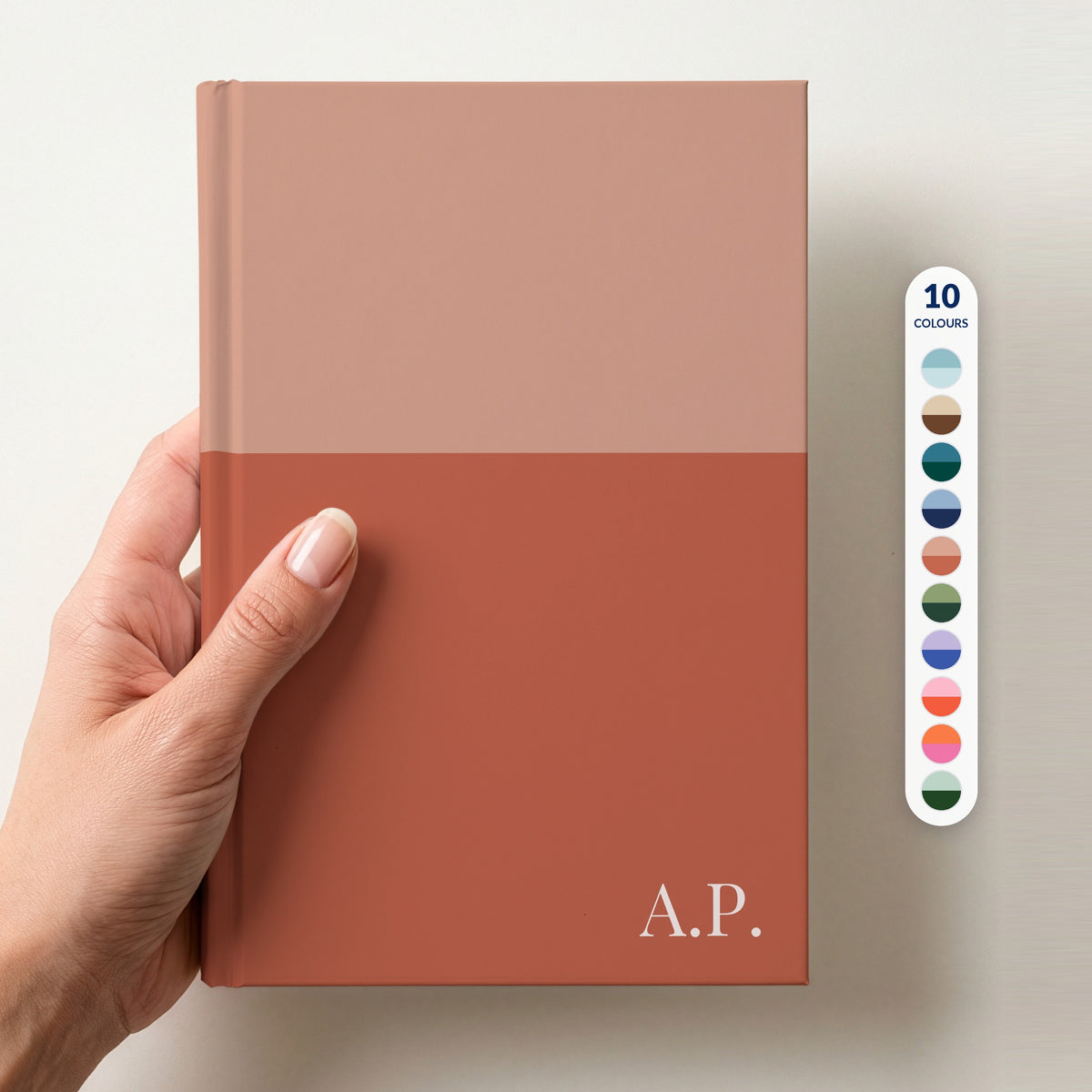 Hand holding a personalised two tone notebook, with a column of ten colour swatches beside it showing the 10 colour combinations available