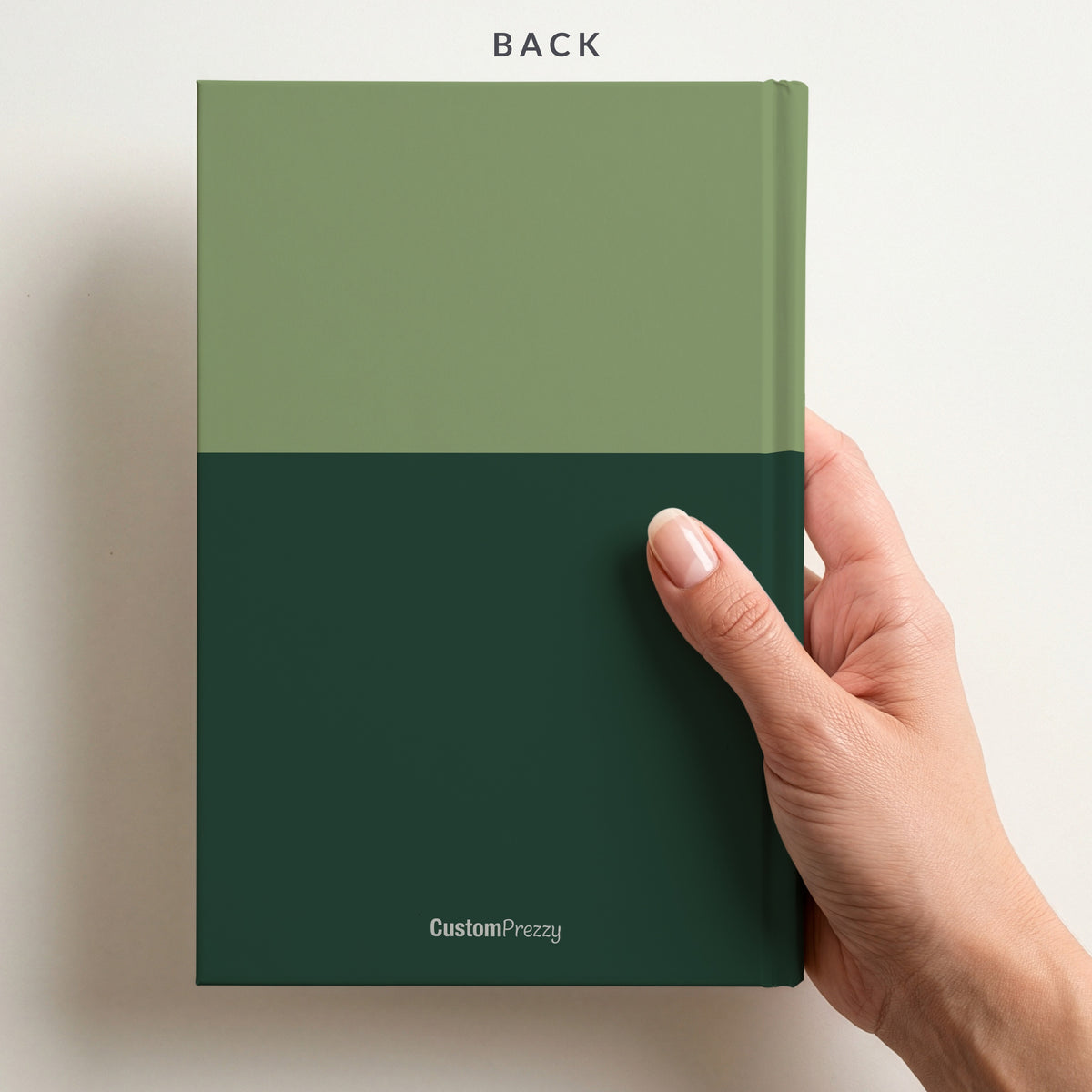 Back of the sage and pine two tone name notebook held in a hand, with the colour split running around the back and the Custom Prezzy wordmark at the foot