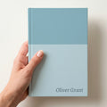 Hand holding a duck egg two tone personalised notebook with the name Oliver Grant in Alegreya in the lower corner