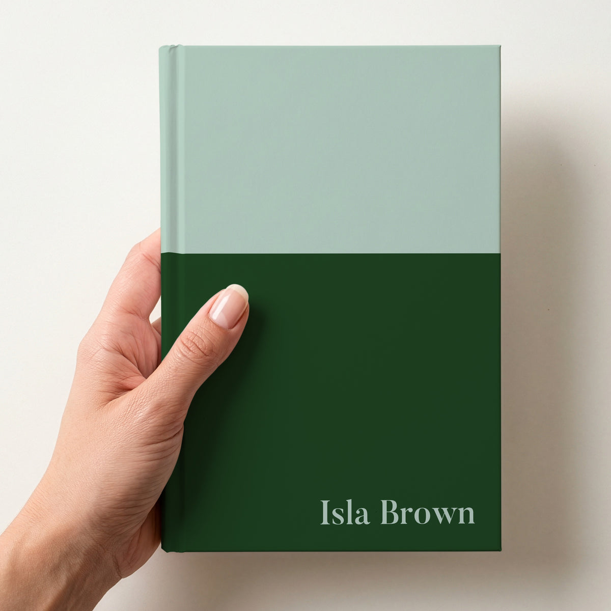 Hand holding a mint and bottle two tone personalised notebook with the name Isla Brown in Butler in the lower corner