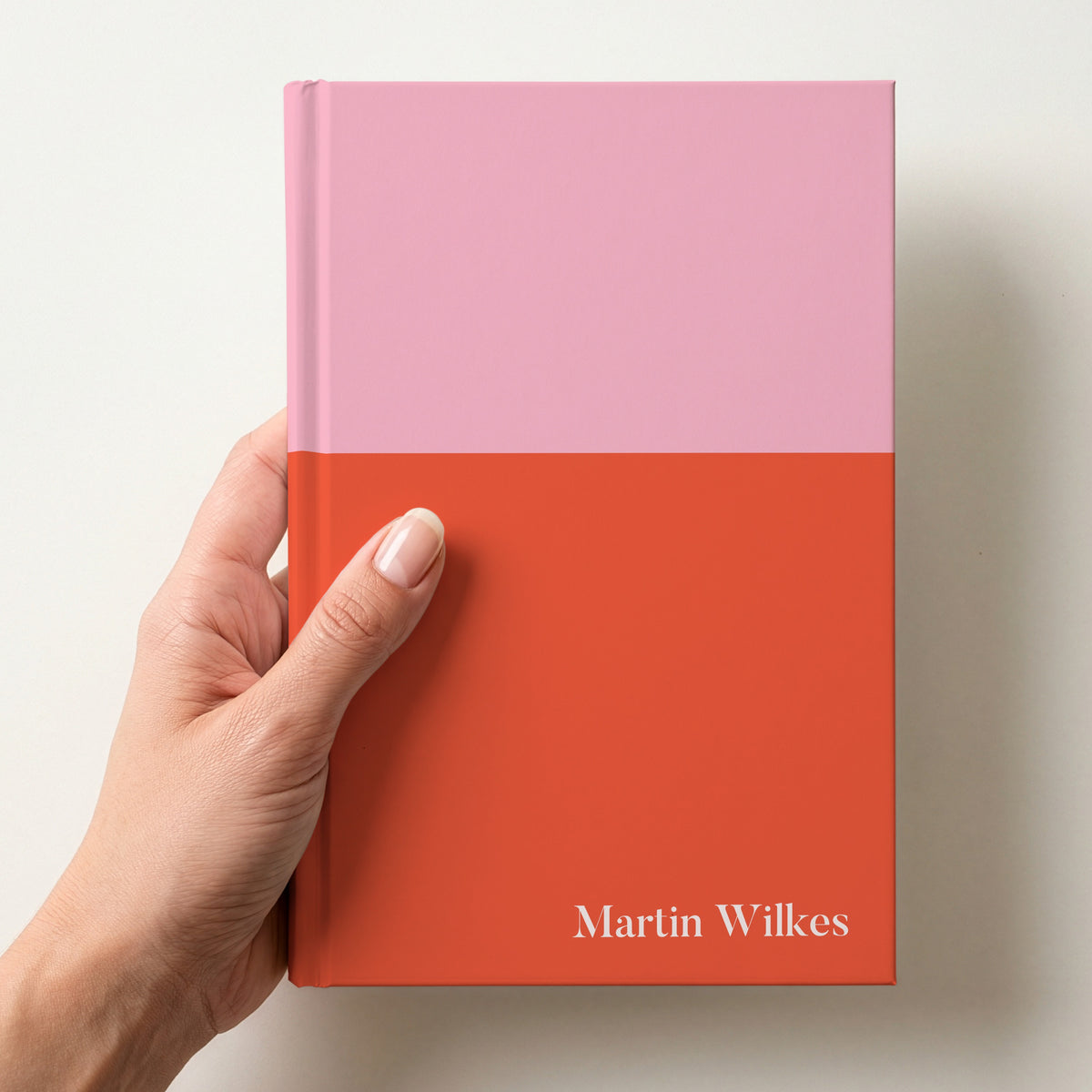 Hand holding a pink and red two tone personalised notebook with the name Martin Wilkes in Butler in the lower corner
