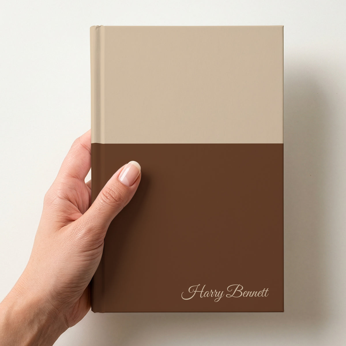 Hand holding a sand and chocolate two tone personalised notebook with the name Harry Bennett in Great Vibes in the lower corner