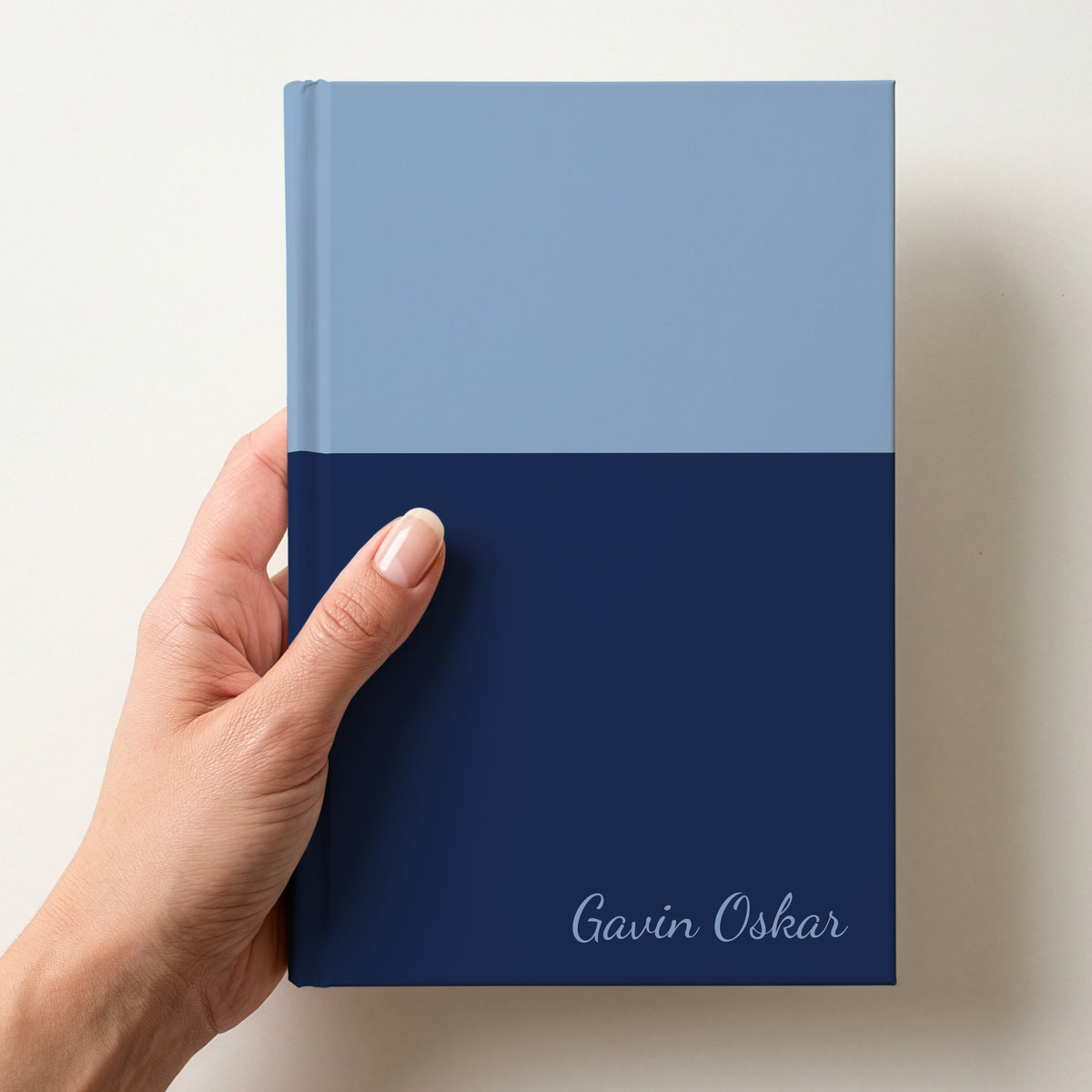 Hand holding a sky and navy two tone personalised notebook with the name Gavin Oskar in Dancing Script in the lower corner