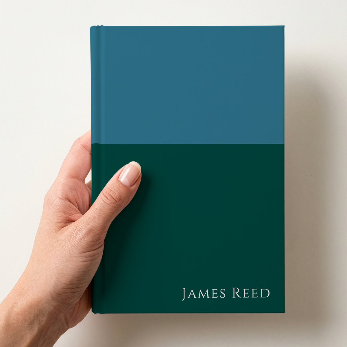 Hand holding a teal and forest two tone personalised notebook with the name James Reed in Cinzel in the lower corner