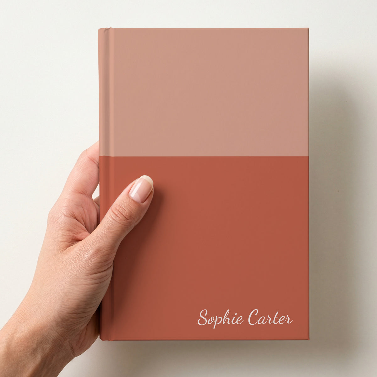 Hand holding a terracotta two tone personalised notebook with the name Sophie Carter in Dancing Script in the lower corner