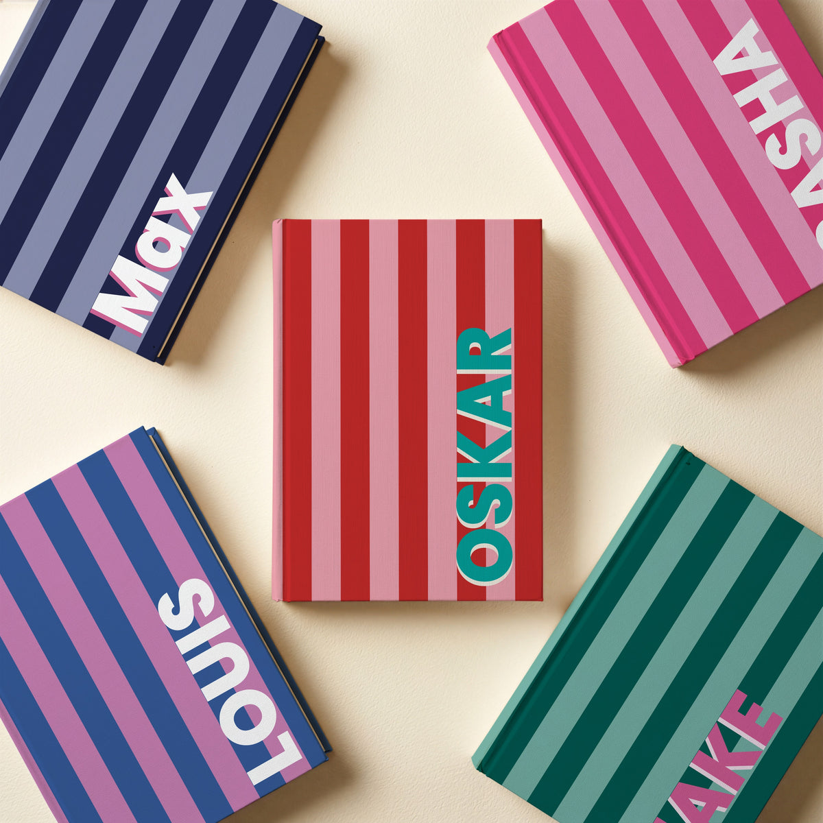All five striped name notebooks laid flat: hot pink, navy, cobalt and orchid, red and pink, and bottle green