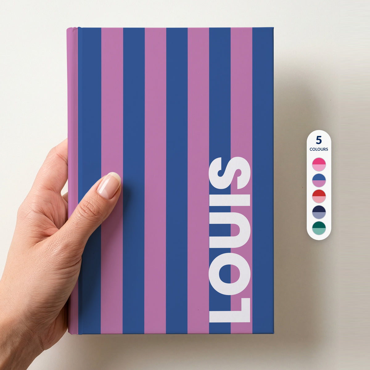 Hand holding a cobalt and orchid striped name notebook, with a column of five colour swatches beside it showing the 5 colourways available