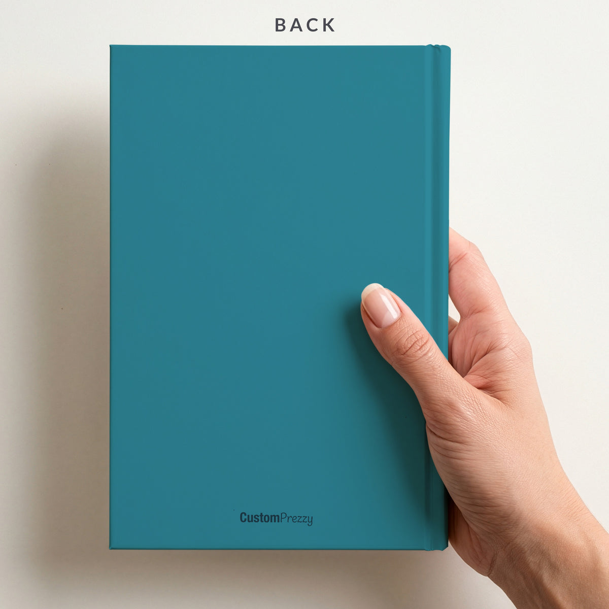 Back of the teal bold block name notebook held in a hand, with the Custom Prezzy wordmark at the foot