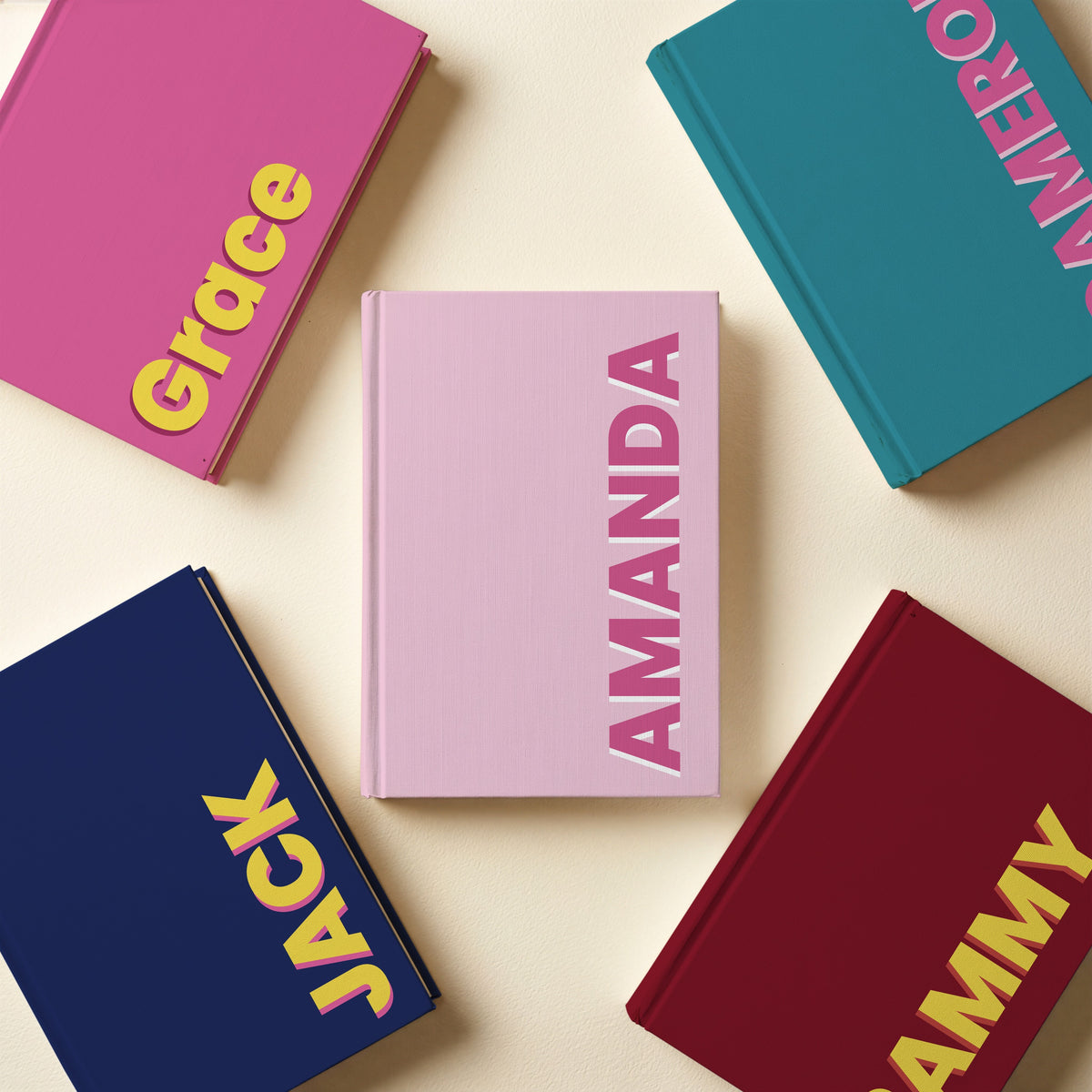 Five bold block name notebooks laid flat in teal, pink, navy, burgundy, light pink