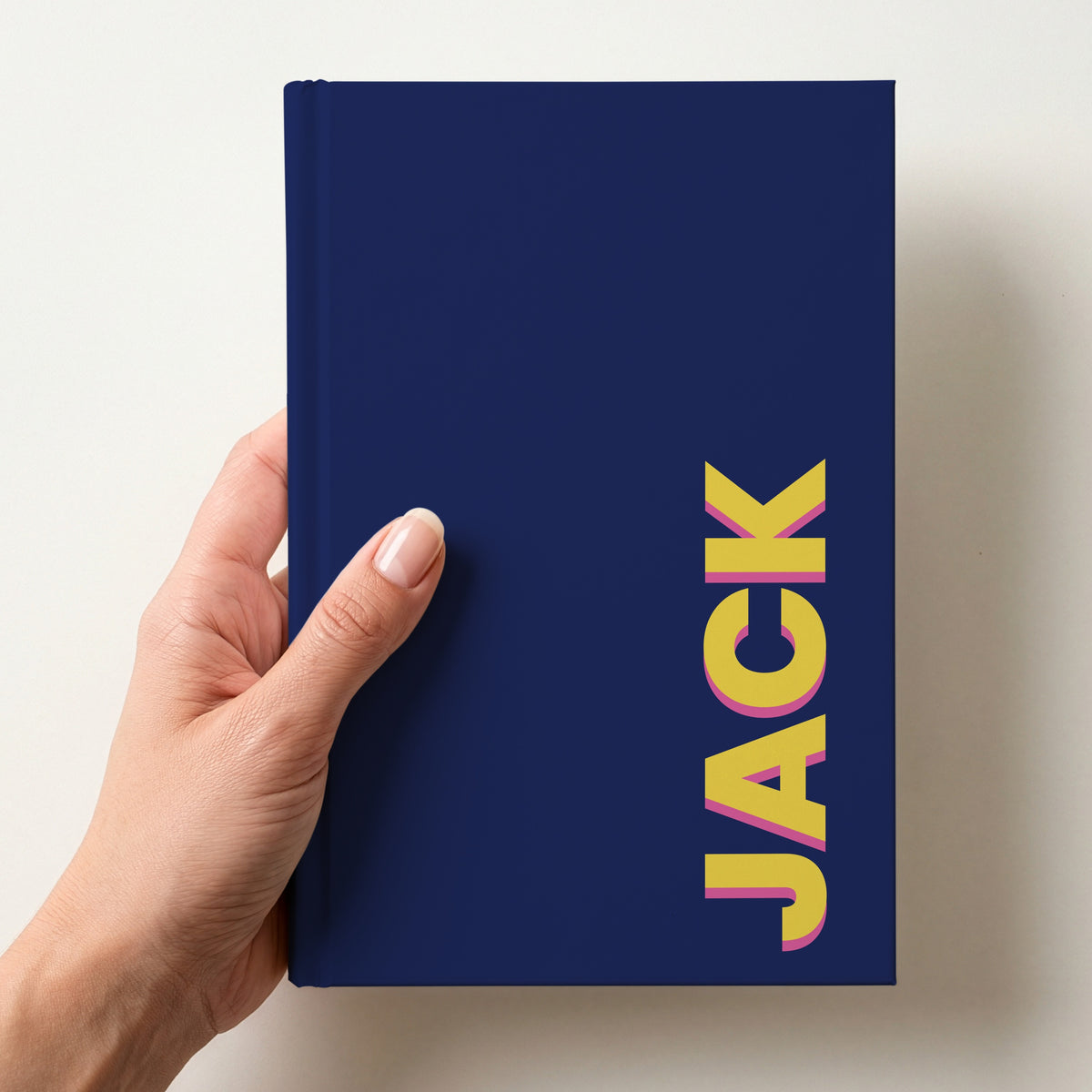 Hand holding a navy notebook with the name JACK in bold block letters running up the right-hand edge