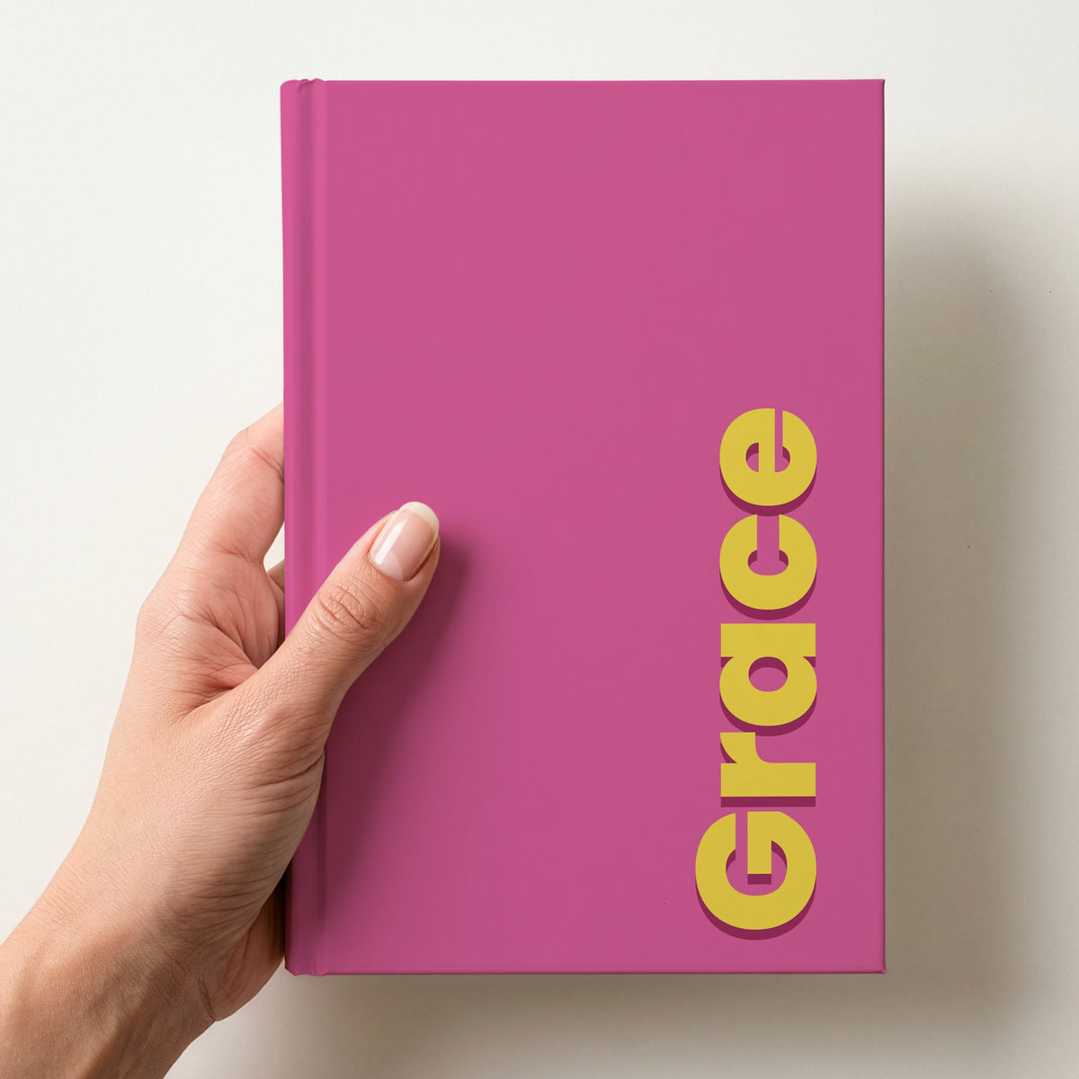 Hand holding a pink notebook with the name Grace in bold block letters running up the right-hand edge