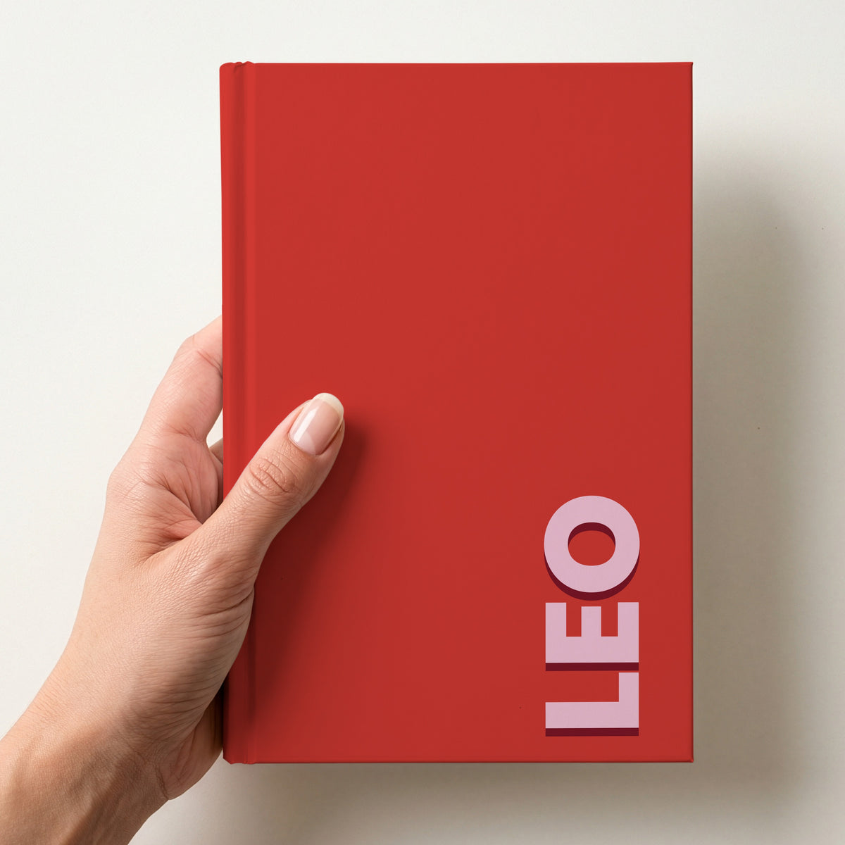 Hand holding a red notebook with the name LEO in bold block letters running up the right-hand edge