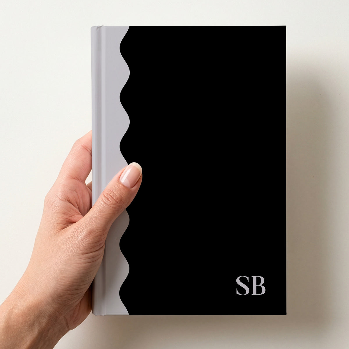 Hand holding a black and grey scalloped colour block notebook with the initials SB in Butler in the lower corner
