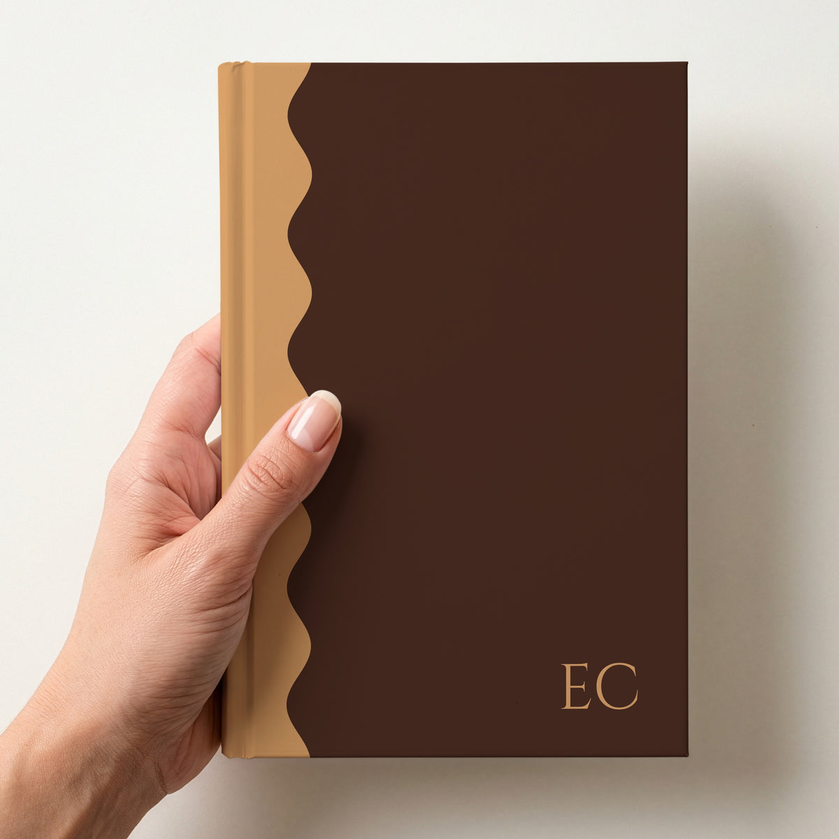 Hand holding a chocolate and caramel scalloped colour block notebook with the initials EC in Cinzel in the lower corner