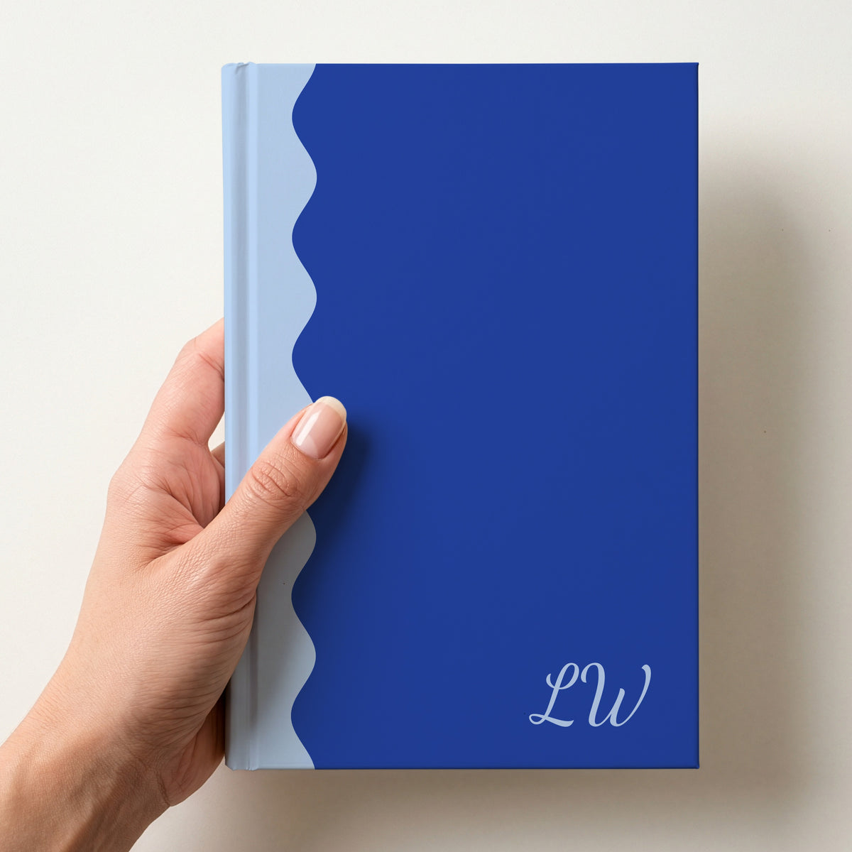 Hand holding a cobalt and sky blue scalloped colour block notebook with the initials LW in Dancing Script in the lower corner