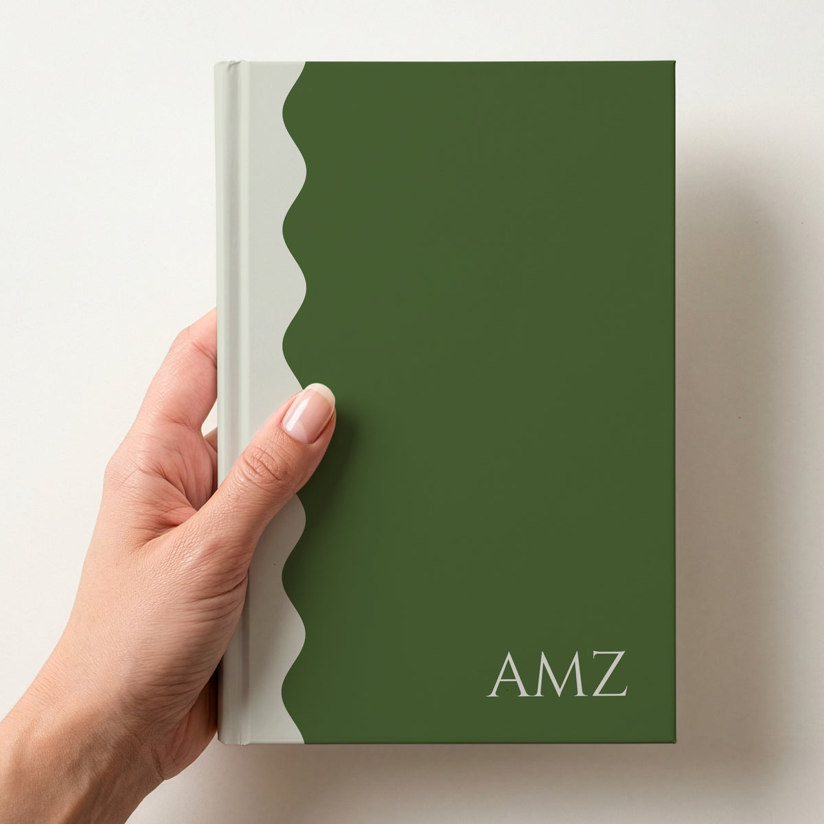 Hand holding a green and cream scalloped colour block notebook with the initials AMZ in Cinzel in the lower corner