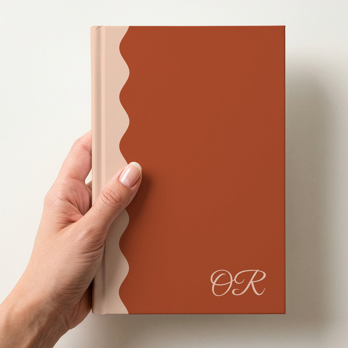 Hand holding a terracotta and peach scalloped colour block notebook with the initials OR in Great Vibes in the lower corner
