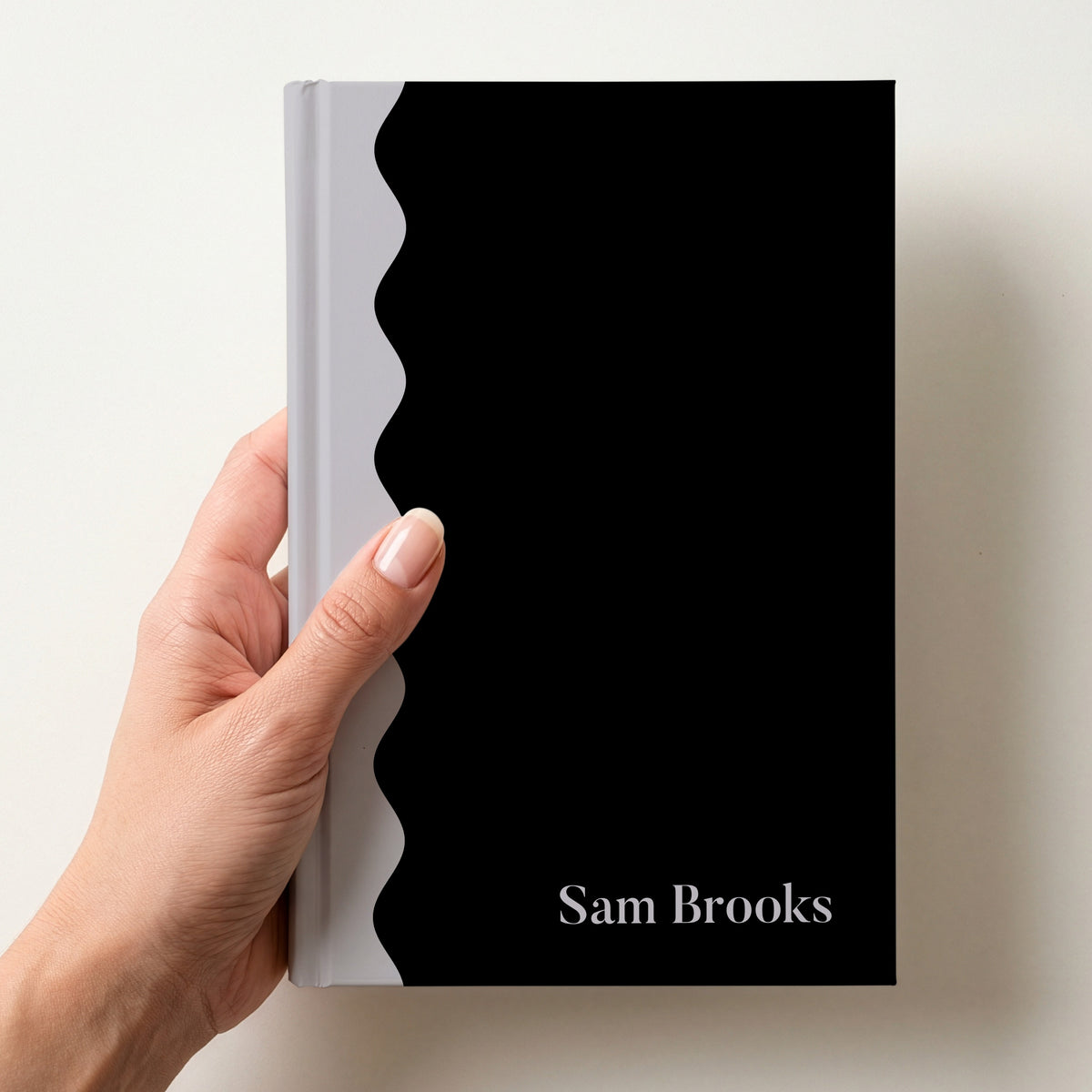 Hand holding a black and grey scalloped colour block notebook with the name Sam Brooks in Butler in the lower corner