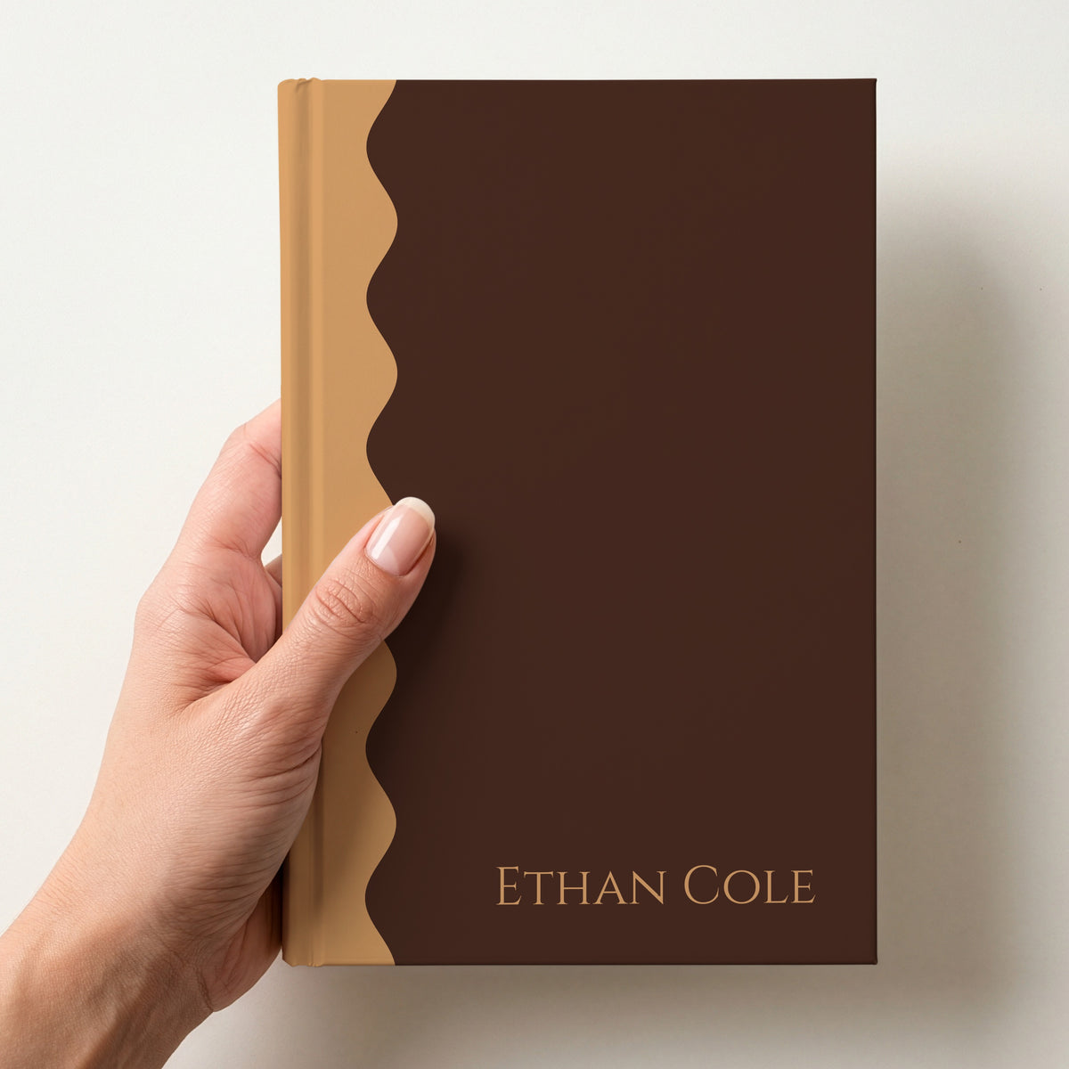 Hand holding a chocolate and caramel scalloped colour block notebook with the name Ethan Cole in Cinzel in the lower corner