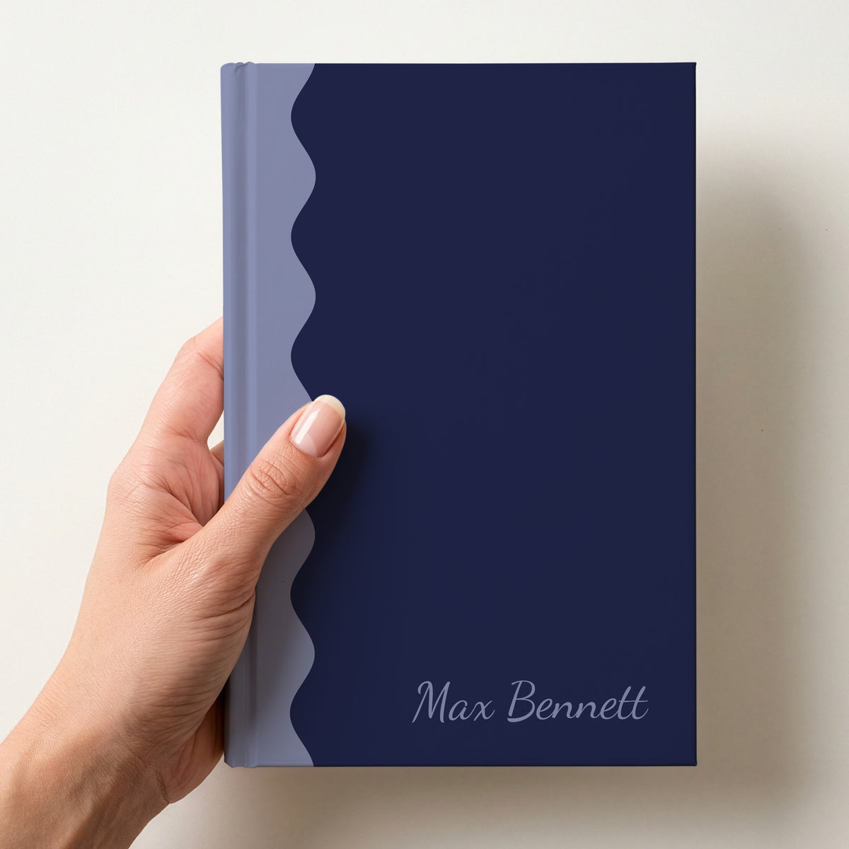 Hand holding a navy and periwinkle scalloped colour block notebook with the name Max Bennett in Dancing Script in the lower corner