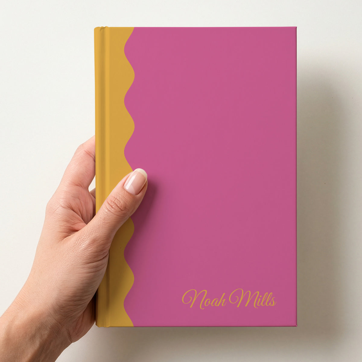 Hand holding a pink and mustard scalloped colour block notebook with the name Noah Mills in Great Vibes in the lower corner