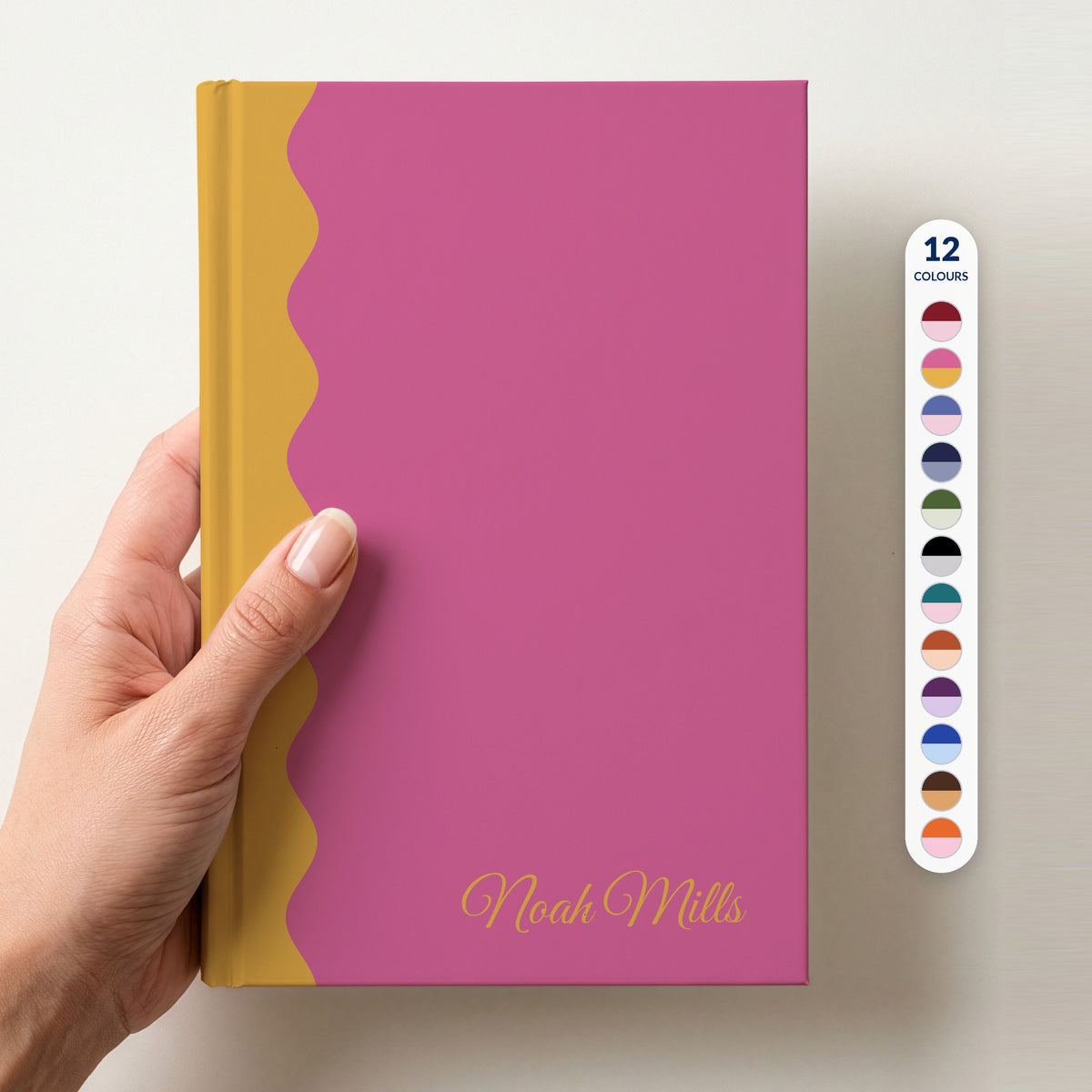 Hand holding a pink and mustard scalloped colour block notebook with the name Noah Mills in Great Vibes in the lower corner, with a column of 12 colour swatches beside it showing all 12 colours