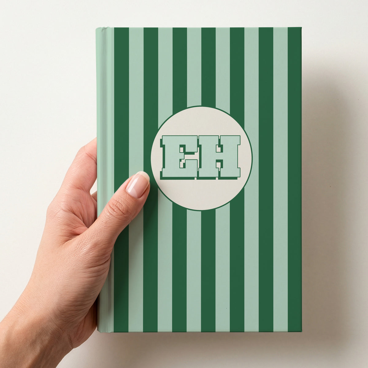 Hand holding a personalised green striped hardcover notebook with retro initials EH