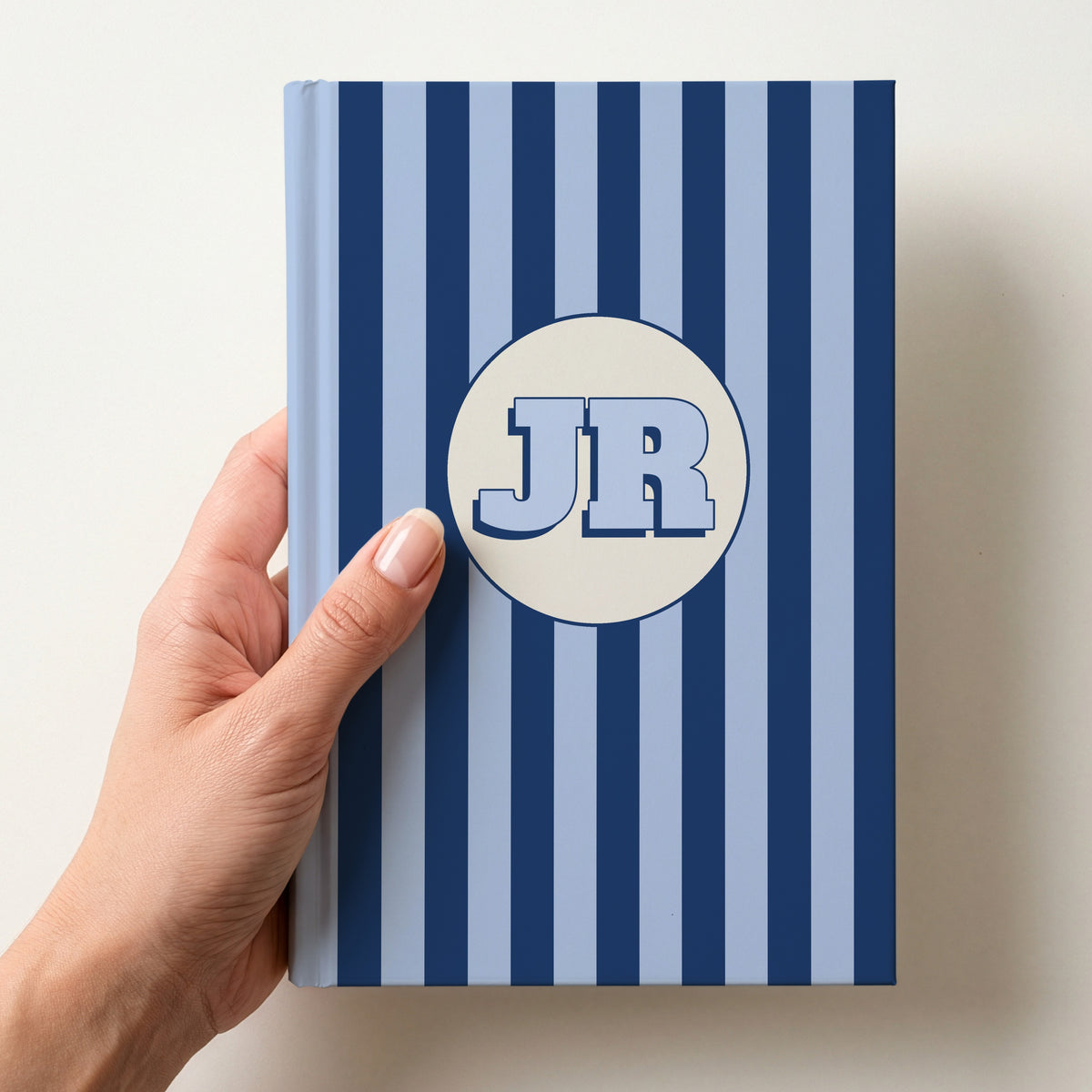 Hand holding a personalised navy striped hardcover notebook with retro initials JR