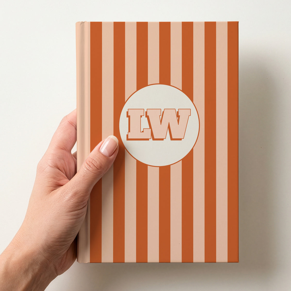 Hand holding a personalised orange striped hardcover notebook with retro initials LW