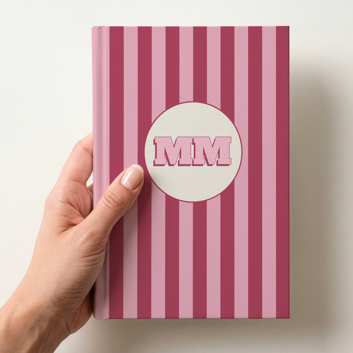 Hand holding a personalised pink striped hardcover notebook with retro initials MM in a cream circle