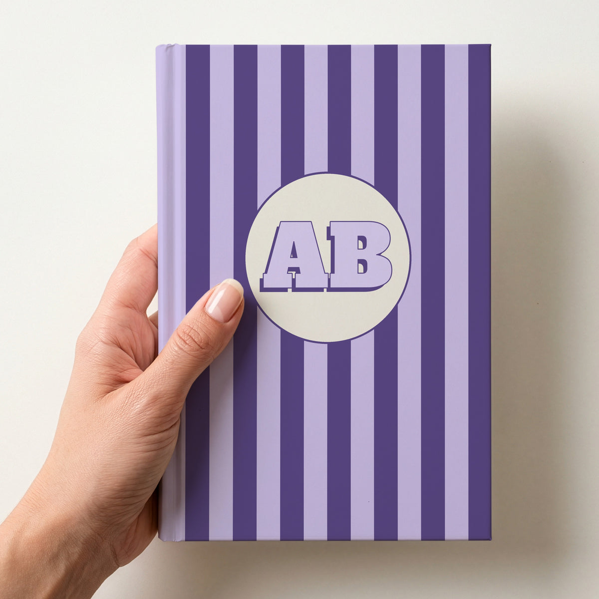 Hand holding a personalised purple striped hardcover notebook with retro initials AB