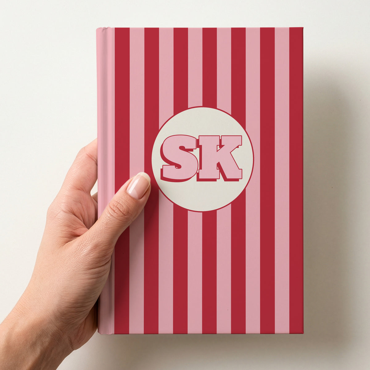 Hand holding a personalised red striped hardcover notebook with retro initials SK