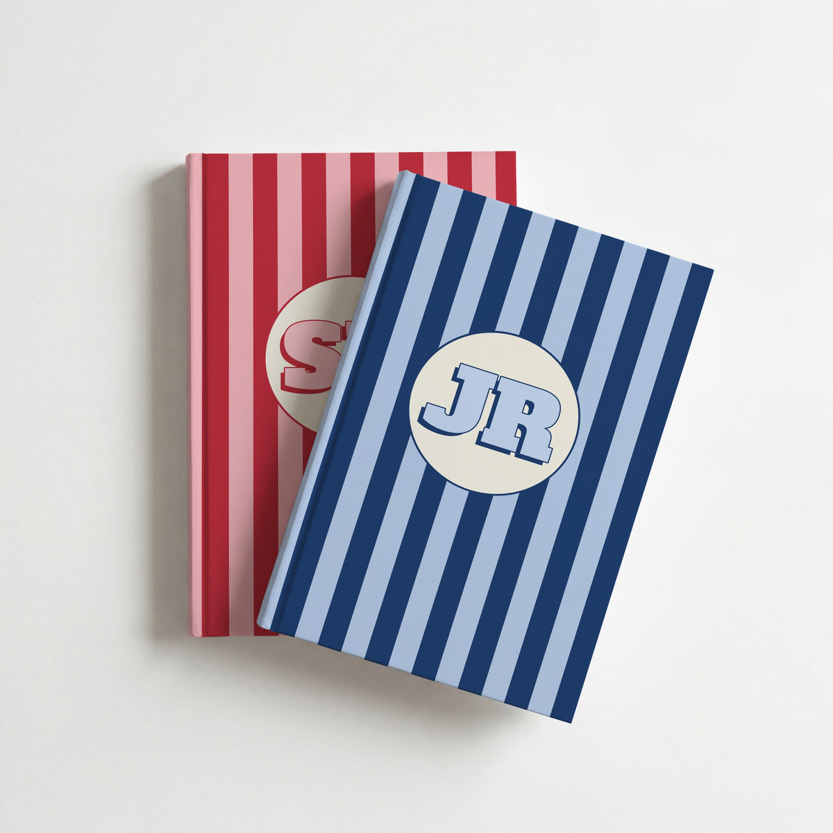 Two personalised striped notebooks, navy with initials JR on top of red, on a white surface