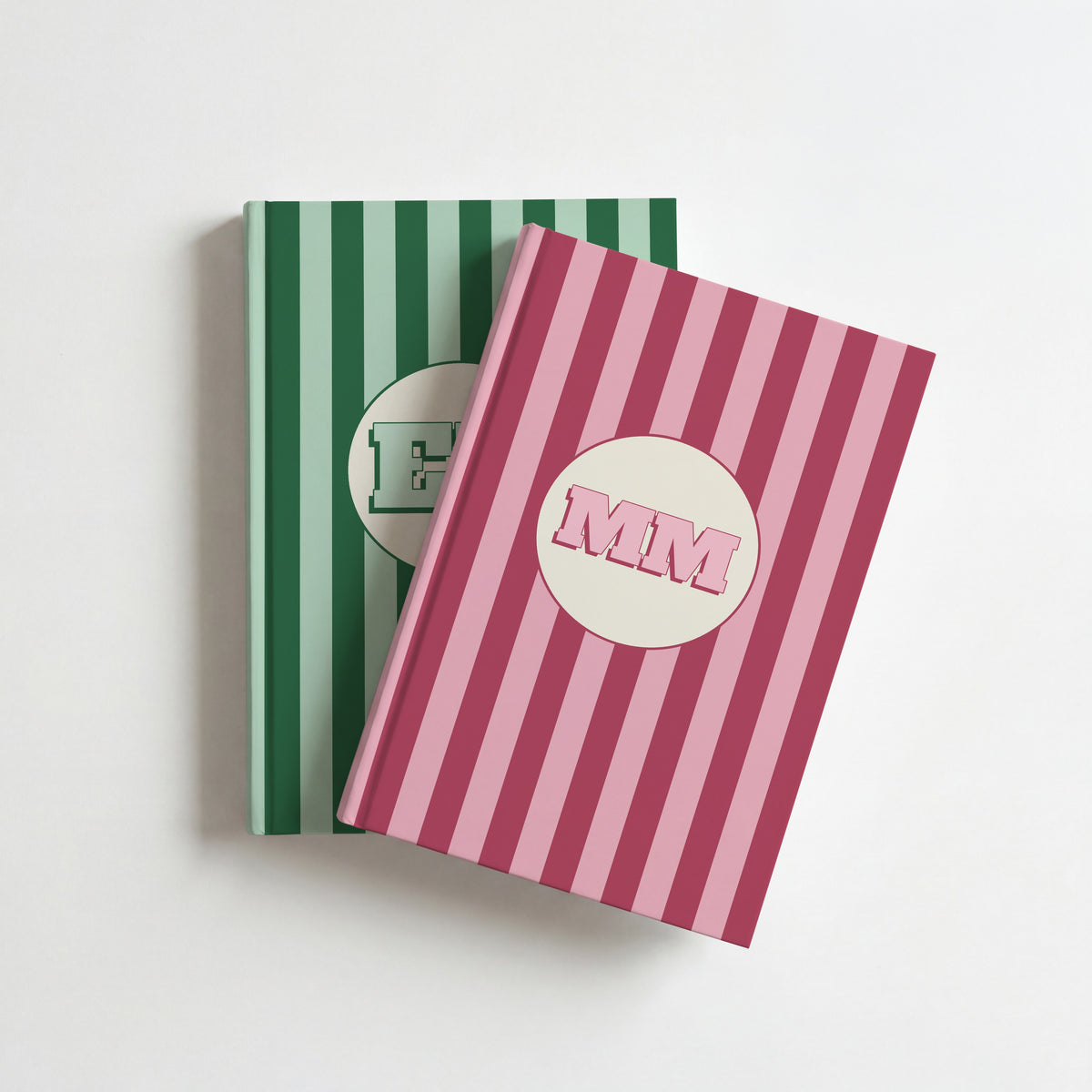Two personalised striped notebooks, pink with initials MM on top of green, on a white surface