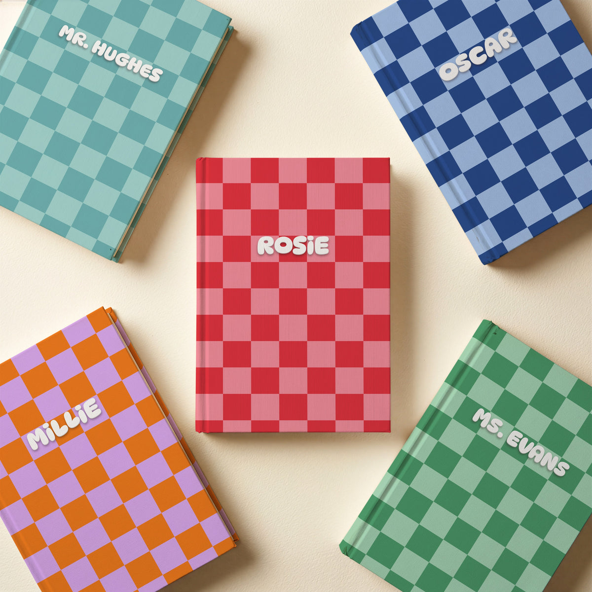 Five personalised checkerboard name notebooks in teal, navy, red, orange and lilac, and green on a cream surface