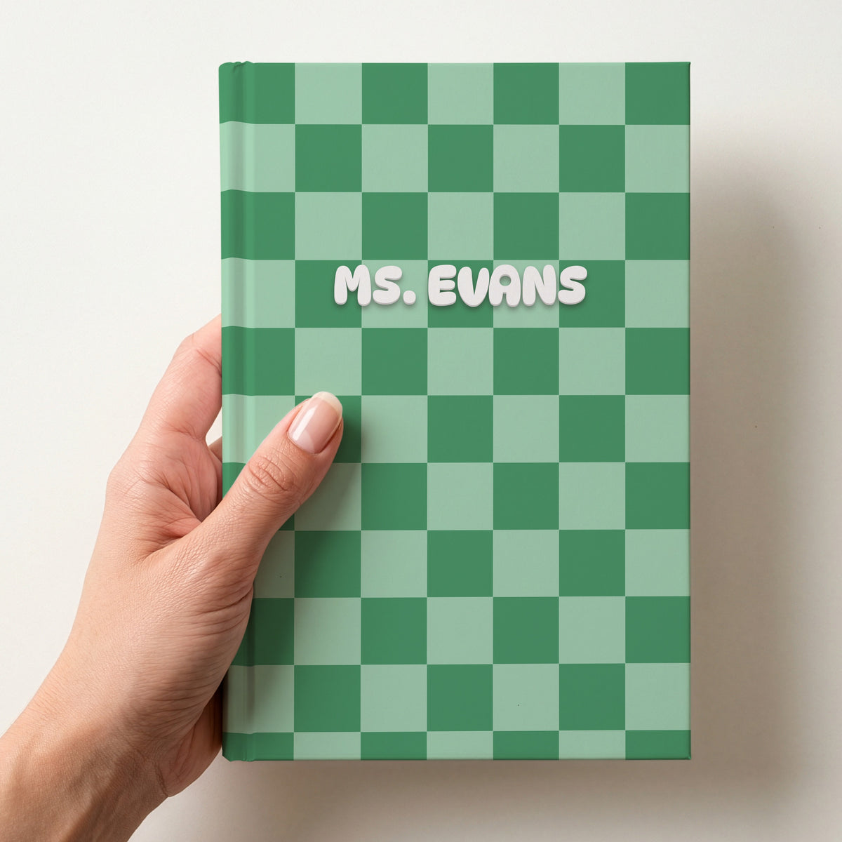 Hand holding a personalised green checkerboard notebook with the name Ms. Evans