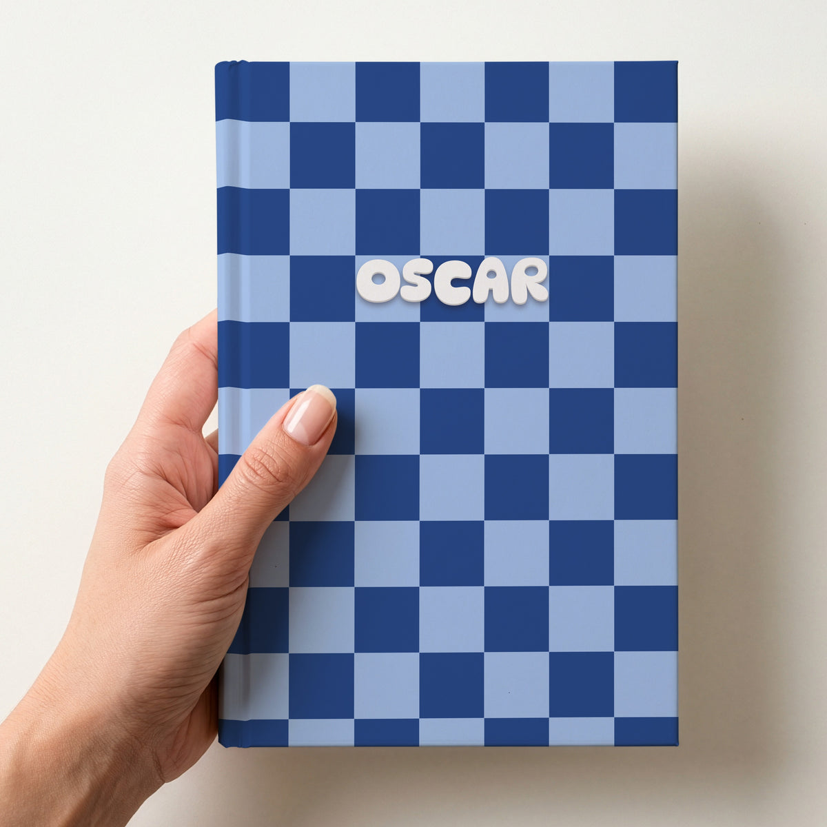 Hand holding a personalised navy and sky blue checkerboard notebook with the name Oscar