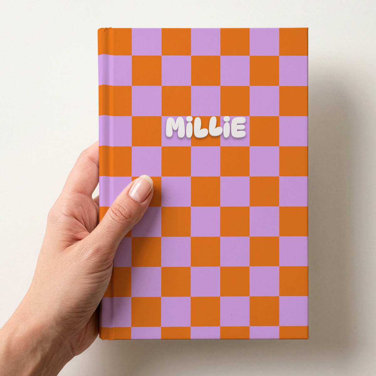 Hand holding a personalised orange and lilac checkerboard notebook with the name Millie