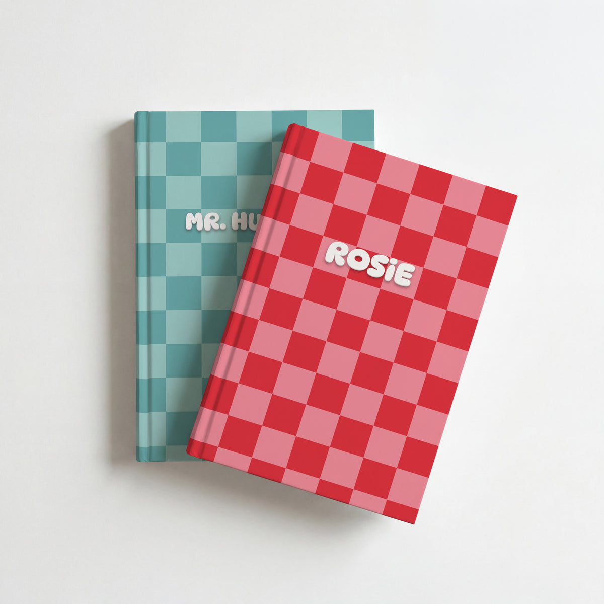 Two personalised checkerboard notebooks, red and pink with the name Rosie on top of teal, on a white surface