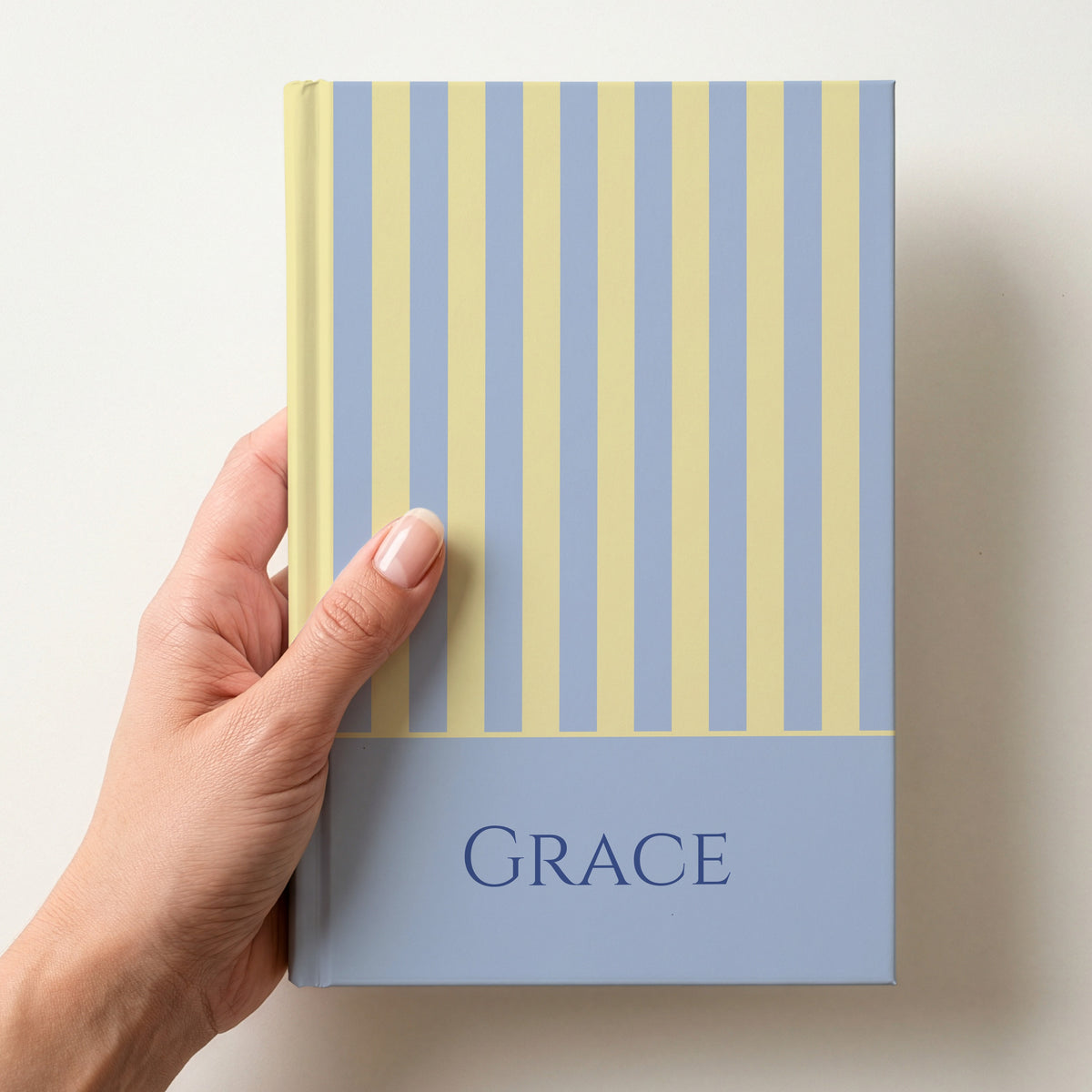 Hand holding a personalised blue and yellow striped notebook with the name Grace in capitals