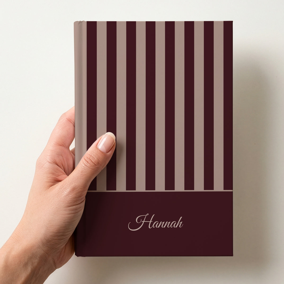 Hand holding a personalised brown and taupe striped notebook with the name Hannah in script