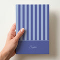Hand holding a personalised blue striped notebook with a dark blue band and the name Sophie in script